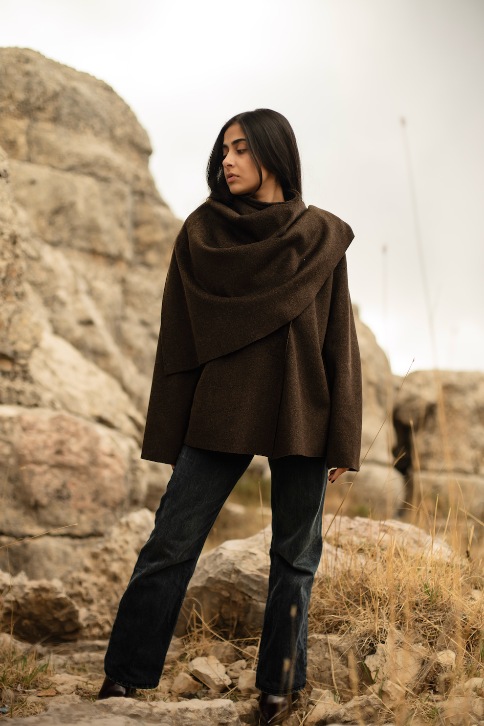 Woman wearing a brown poncho standing in a rocky, desert-like landscape