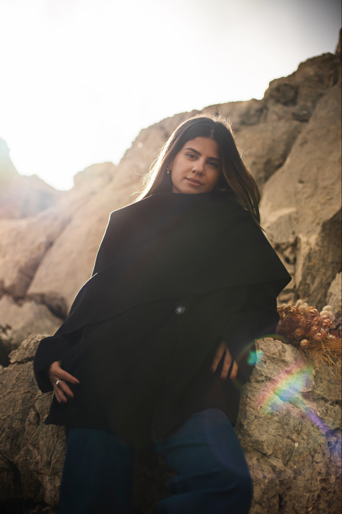 Person wearing a black coat standing on rocky terrain with a rainbow in the background
