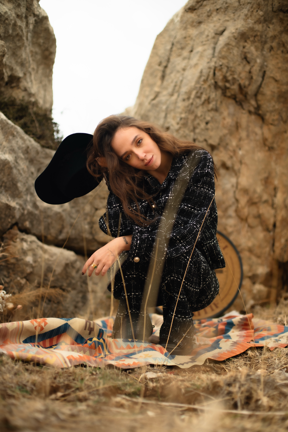 Woman wearing tweed setin a natural setting with rocks and a blanket.