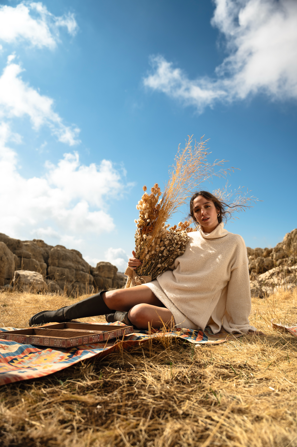 Woman sitting on a blanket with dried plants against a blue sky