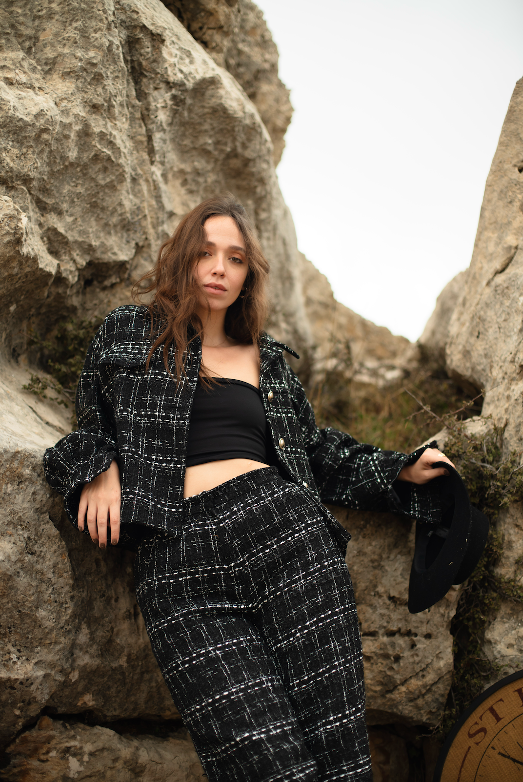 Woman in a black and white checkered outfit standing against rocky cliffs.
